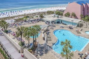 A resort with a swimming pool, beach area, and a pink building.