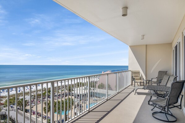 Un balcone con vista sulla spiaggia e sull'oceano, arredato con sedie e un tavolo.