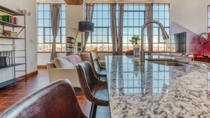 A spacious living area with a large window, a kitchen island, and a seating area with a sofa and chairs. - Sosuite 2BR Penthouse w Balcony W D Gym (Philadelphia)