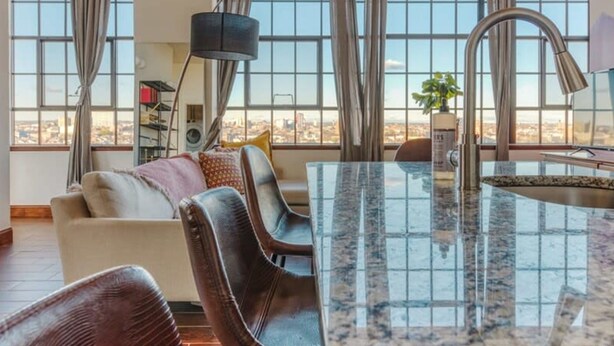 A spacious living area with a large window, a kitchen island, and a seating area with a sofa and chairs. - Sosuite 2BR Penthouse w Balcony W D Gym (Philadelphia)