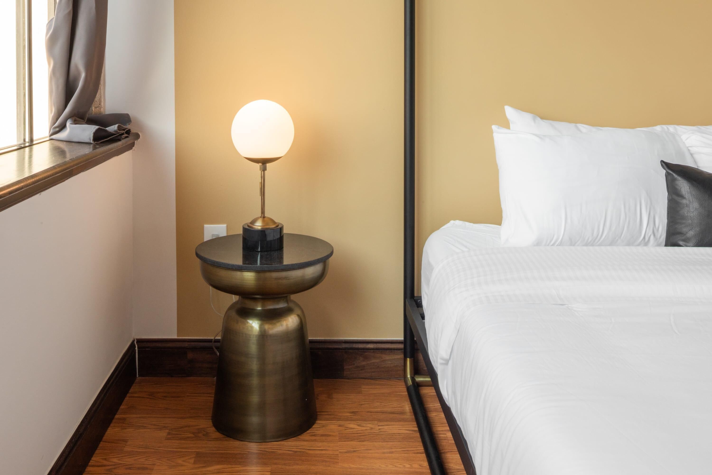 Une chambre d’hôtel avec un lit, une table de chevet avec une lampe et une fenêtre avec des rideaux.