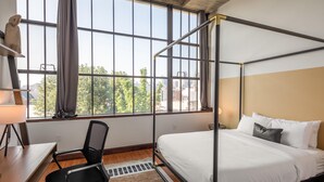 A modern room with a metal bed frame, a desk with a chair, and a large window offering a city view. - Sosuite 2BR Apt w Balcony, W/d, Gym, On-site Bar (Philadelphia)