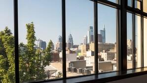 A view through large windows of a cityscape with various buildings, including a distinctive skyscraper with a spire. - Sosuite 2BR Apt w Balcony, W/d, Gym, On-site Bar (Philadelphia)