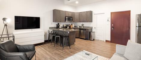 A modern kitchen with a central island, bar stools, and a flat-screen TV.