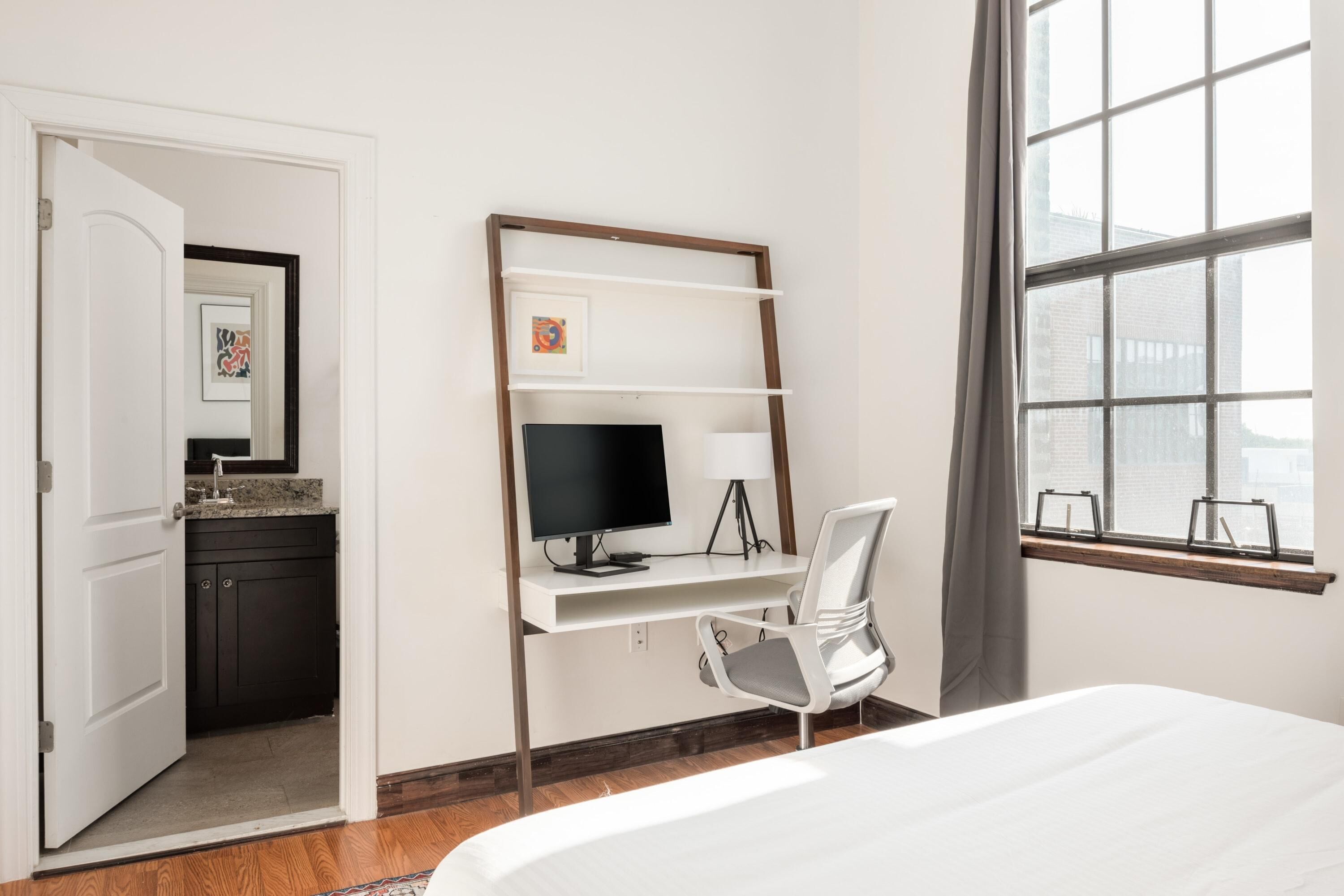 Una habitación de hotel con escritorio, una silla, una cama, un ventanal y vistas al exterior.