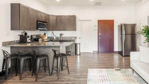 A modern kitchen with dark cabinets, a stainless steel refrigerator, and a bar area with stools. - Sosuite 2BR Apt w Balcony, W/d, Gym, On-site Bar (Philadelphia)
