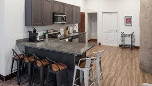 A modern kitchen with dark cabinets, a granite countertop, and a central island with bar stools. - Sosuite 3BR Apt w Balcony, W/d, Gym, On-site Bar (Philadelphia)