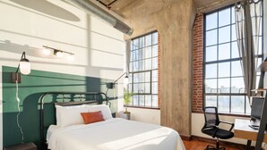 A bedroom with a bed, a desk, and a chair. There are windows with curtains, a plant on the desk, and a radiator on the wall. - Sosuite 3BR Apt w Balcony, W/d, Gym, On-site Bar (Philadelphia)