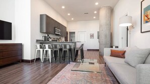A modern kitchen with bar stools, a dining area, and a living room with a sofa and a coffee table. - Sosuite 3BR Apt w Balcony, W/d, Gym, On-site Bar (Philadelphia)