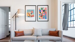 A modern living room with a grey sofa, a glass coffee table, and two abstract paintings on the wall. - Sosuite 3BR Apt w Balcony, W/d, Gym, On-site Bar (Philadelphia)