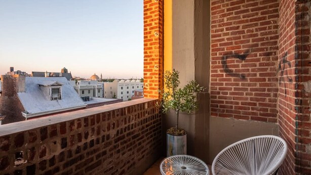 A balcony with two white wire chairs, a potted plant, and a view of the cityscape. - Sosuite 3BR Apt w Balcony, W/d, Gym, On-site Bar (Philadelphia)