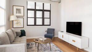 A modern living room with a sofa, armchair, coffee table, TV, and framed artwork on the wall. - Sosuite Corner 1BR Apt w W/d, Shared Roofdeck (Philadelphia)