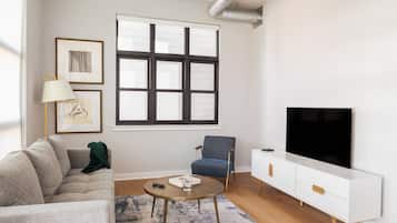 A modern living room with a sofa, armchair, coffee table, TV, and framed artwork on the wall.