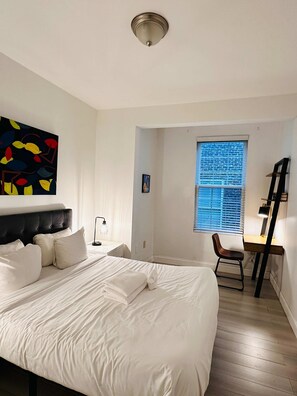 A bedroom with a large bed, a desk, a chair, a window with blinds, and a ceiling light. - Cherry Suites 2BR Apt w W D Arcade Machine (Philadelphia)