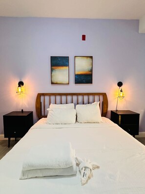 A neatly made bed with white linens and pillows, two bedside tables with lamps, and two abstract paintings on the wall. - Cherry Suites 2BR Apt w W D Arcade Machine (Philadelphia)