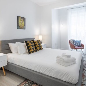 A modern hotel room with a large bed, a bedside table, a chair, and a window with curtains. - Cherry Suites 2BR Apt w W D Arcade Machine (Philadelphia)