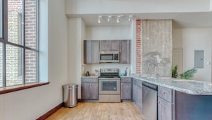 A modern kitchen with a built-in oven, microwave, and dishwasher, wooden flooring, and a window with a view of a brick building. - Sosuite 2BR Penthouse w W D Gym On-site Bar (Philadelphia)