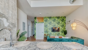 A modern kitchen with granite countertops, a built-in sink, and a dining area with a teal sofa and a TV mounted on the wall. - Sosuite 2BR Penthouse w W D Gym On-site Bar (Philadelphia)