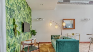 A modern living room with a teal sofa, a wooden chair, a flat-screen TV, and a wall with a leafy pattern. - Sosuite 2BR Penthouse w W D Gym On-site Bar (Philadelphia)