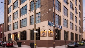 A multi-story building with a corner entrance, large windows, and a street-level sign advertising a new apartment. - Sosuite 2BR Penthouse w W D Gym On-site Bar (Philadelphia)