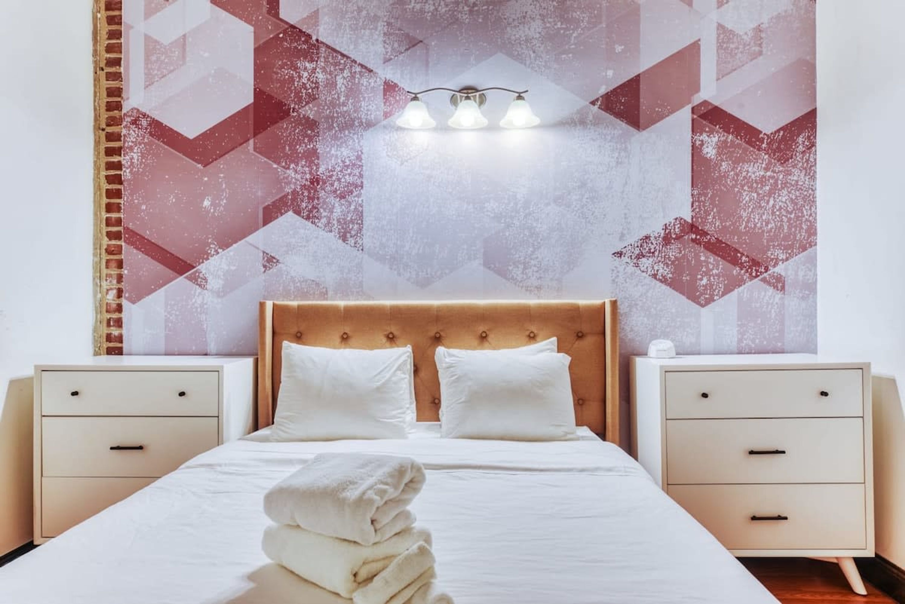 Une chambre d’hôtel avec un lit, deux tables de chevet et un mur orné de motifs géométriques.