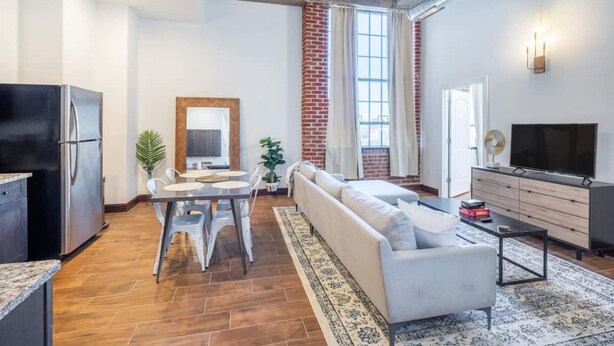 A modern living room with a sofa, dining table, and chairs. There is a TV and a refrigerator in the room. - Sosuite 2BR Penthouse w W D Gym On-site Bar (Philadelphia)