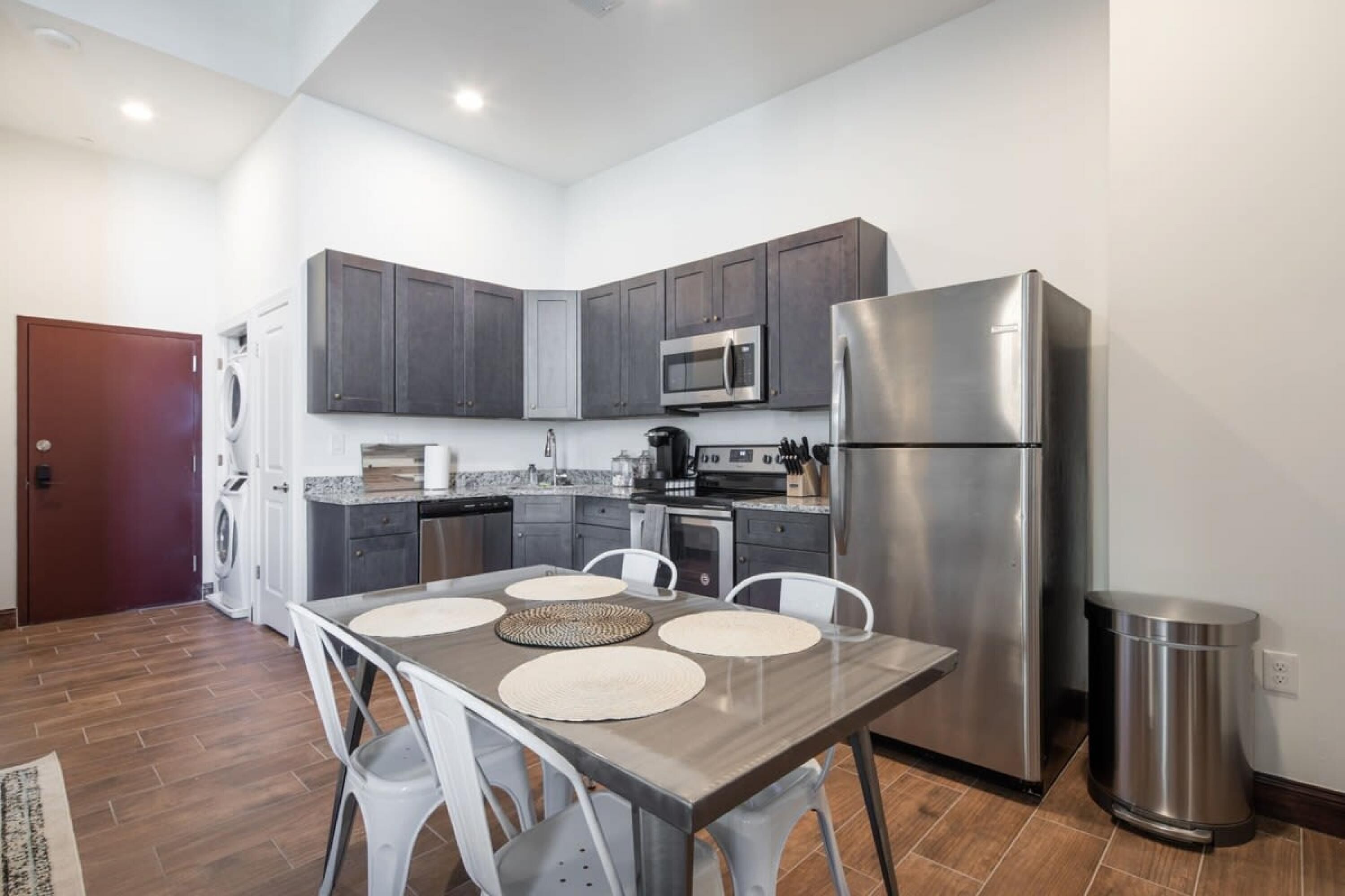A modern kitchen with dark cabinets, stainless steel appliances, and a dining area with a table and chairs.
