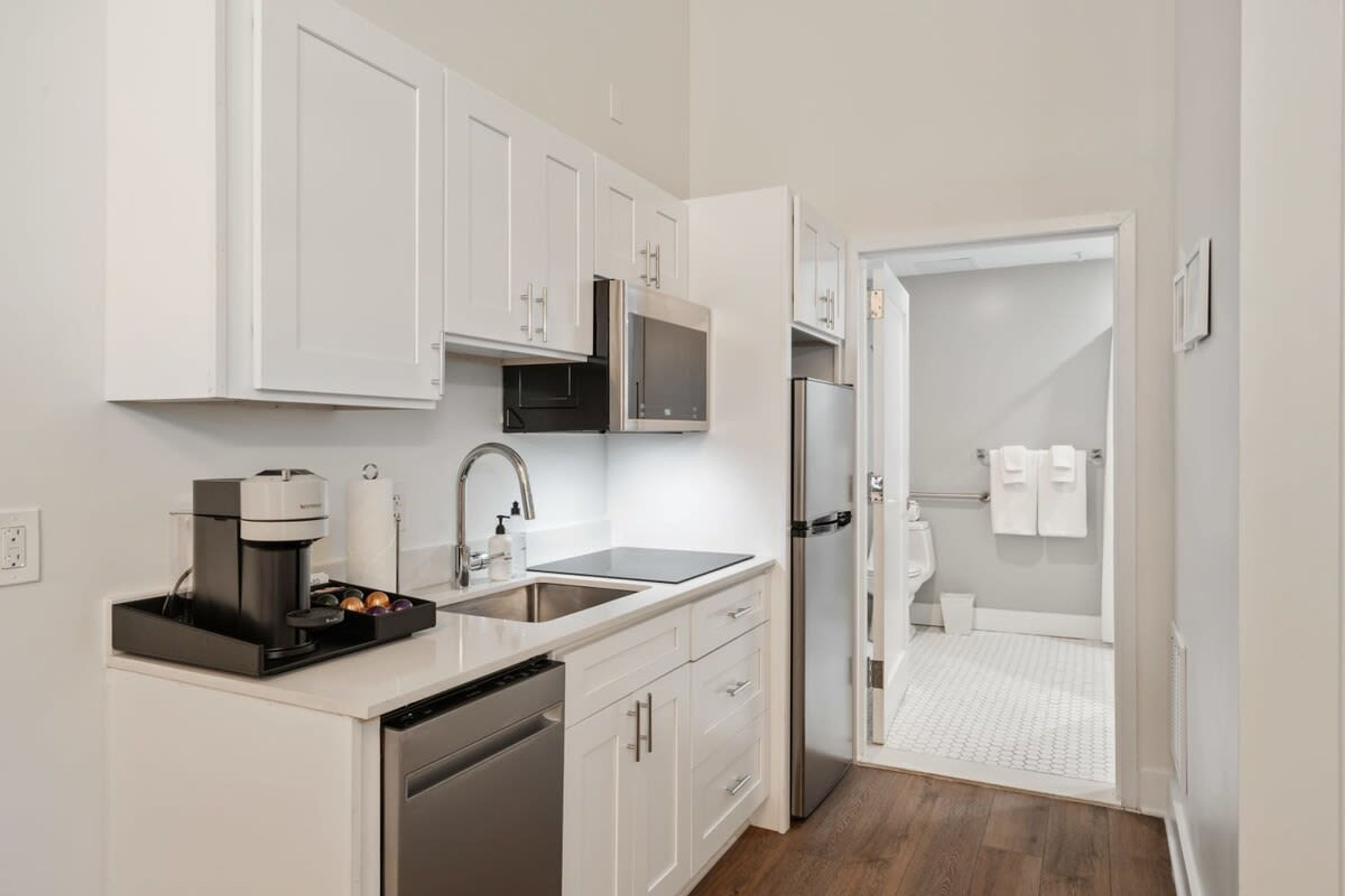 A modern kitchen with white cabinets, a coffee machine, a sink, and a refrigerator.