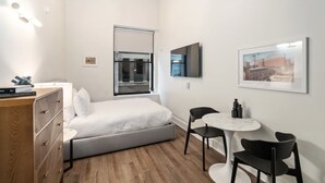 A modern bedroom with a bed, a desk, and a chair. There is a window with a view of buildings outside. - Sosuite Studio Acc. w Shared W/d, Gym, Lounge (Philadelphia)