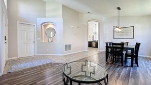 A spacious living room with a glass coffee table, a dining area with a table and chairs, and a kitchen in the background.