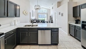 A modern kitchen with dark cabinetry, a central island with a dishwasher, and a large window providing natural light.