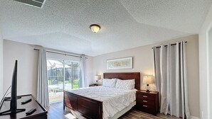 A bedroom with a bed, bedside tables, a TV stand, and a window with curtains.