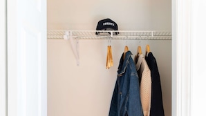 Een kast met hangende kleding en een koffer op de vloer.