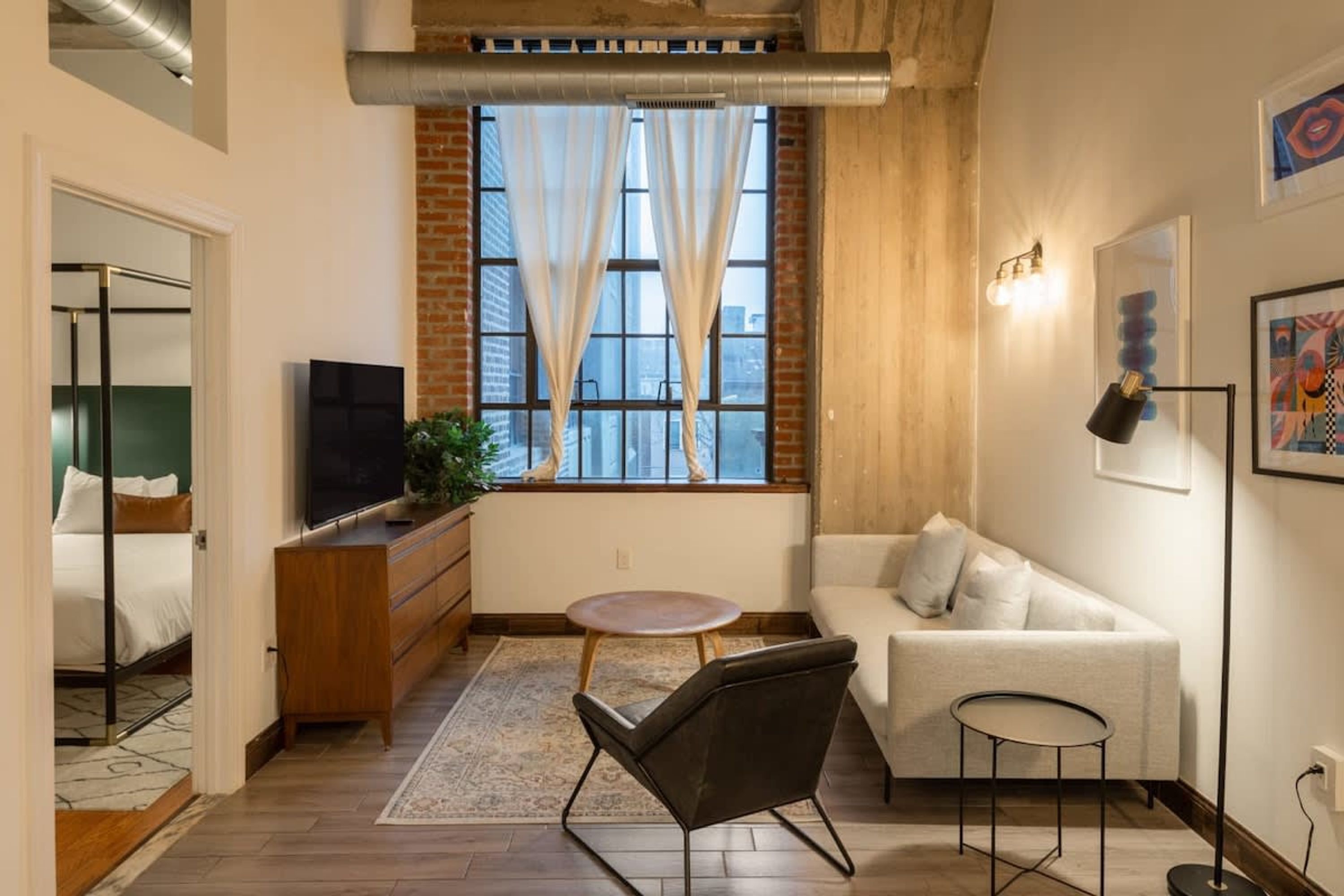 A compact living space with a sofa, a small round table, a TV, and a window with curtains.