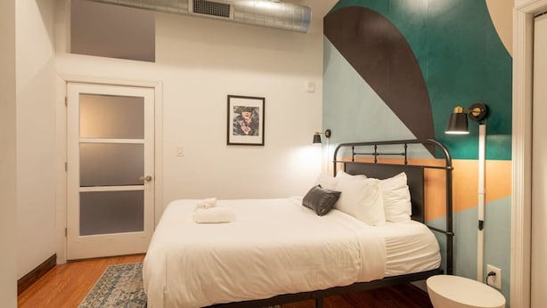 Een slaapkamer met een bed, een wit toilet, een lijst met een foto en een moderne lamp.