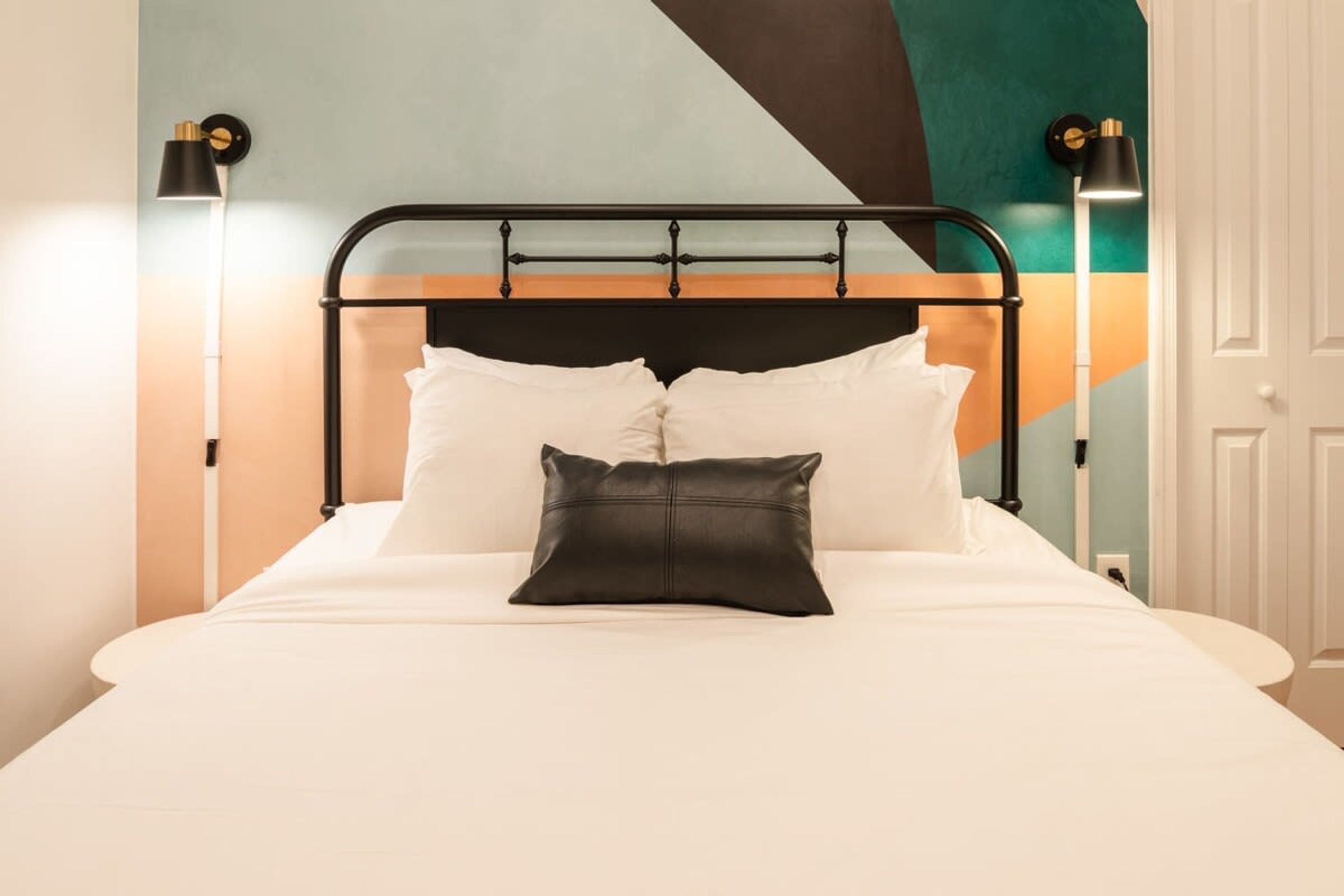 A bed with a black metal frame, white bedding, and a black pillow. There are two wall-mounted lamps on either side of the bed.
