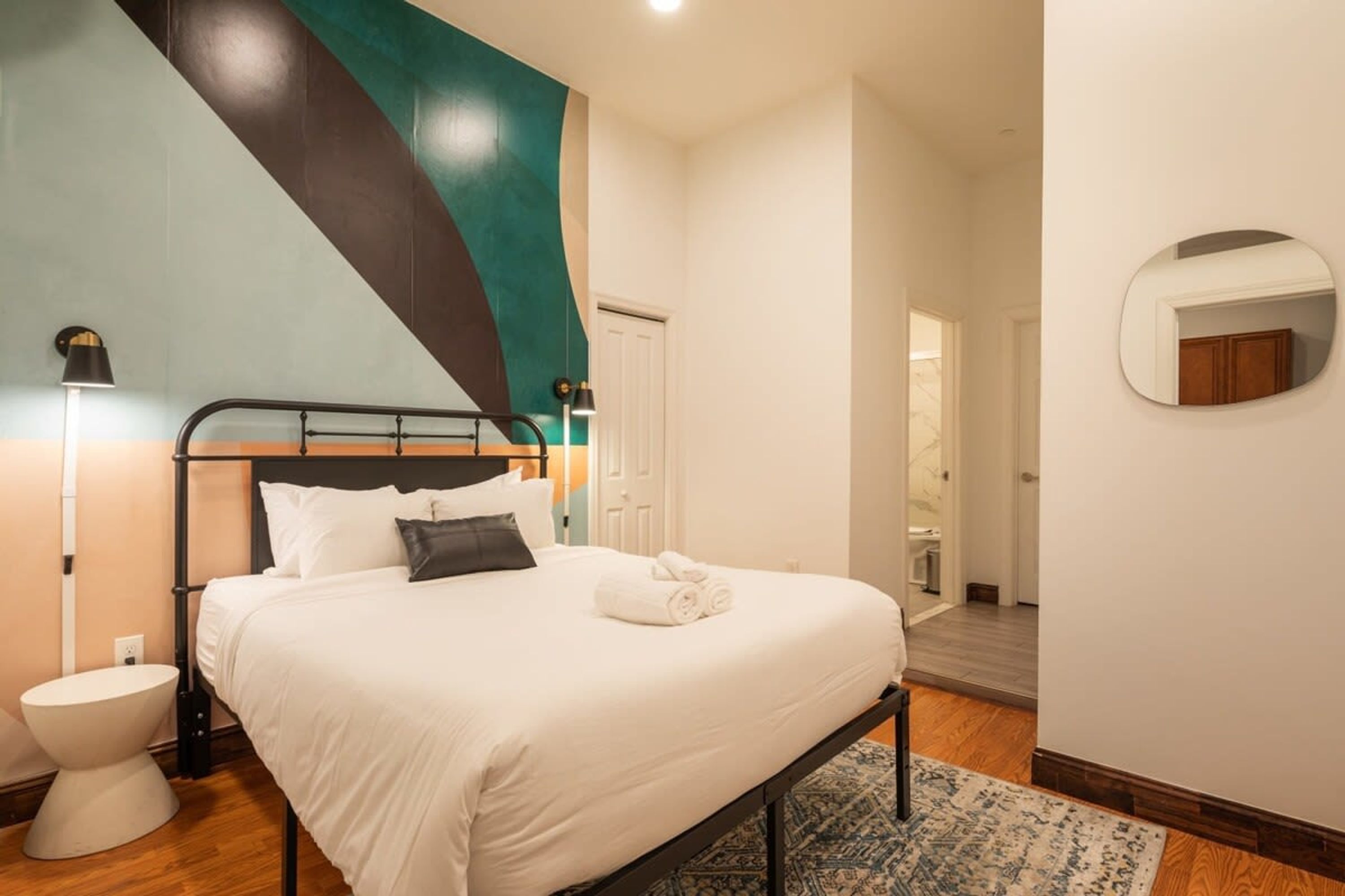 A modern bedroom with a bed, bedside lamp, and a mirror on the wall.