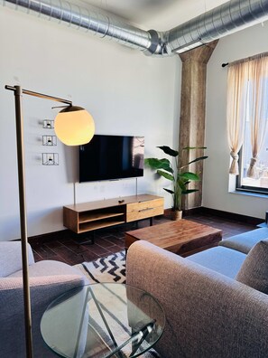 A modern living room with a flat-screen TV, wooden furniture, a glass coffee table, and a potted plant.