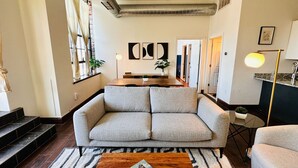 A modern living room with a grey sofa, wooden coffee table, and a dining area with a wooden table and chairs.