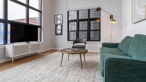 Een moderne woonkamer met een groot raam, een televisie, een groene bank en een ronde salontafel.