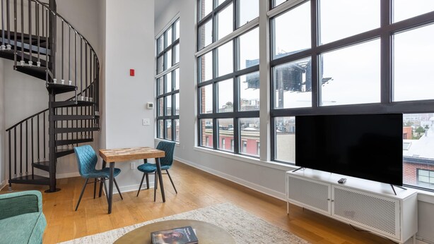 Een ruime woonkamer met een groot raam, een zwarte televisie, een houten tafel en een blauwe stoel.
