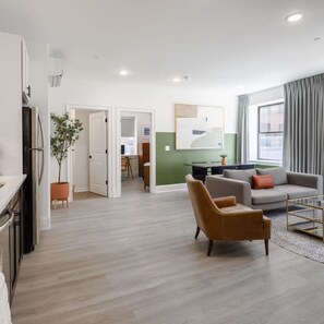 A modern living room with a sofa, armchair, and a coffee table. There is a dining area in the background with a table and chairs. - Sosuite Corner 1BR Apt w W D Desk (Philadelphia)