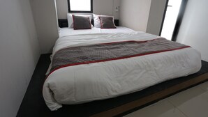 A neatly made bed with white bedding and a red accent, a window with blinds, and a plain wall. - Collection O 93750 Luxury Rooms @ Urbantown Serpong (South Tangerang)