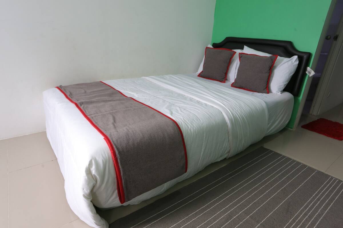 A neatly made bed with a white and gray bedspread, red trim, and two pillows.