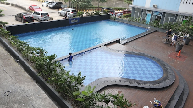 A swimming pool with a checkered pattern, surrounded by greenery and a parking area with several cars. - Collection O 93750 Luxury Rooms @ Urbantown Serpong (South Tangerang)