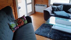 A cozy room with a wooden interior, featuring a sofa, a glass coffee table, and a window with a view of the outdoors. - Urlaub in der Meise (Winsen (Aller))