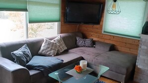 A cozy living room with a sofa, a glass coffee table, and a television mounted on the wall. - Urlaub in der Meise (Winsen (Aller))