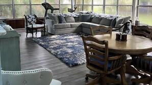 A spacious living room with a large sectional sofa, a dining table with chairs, and a blue patterned rug.