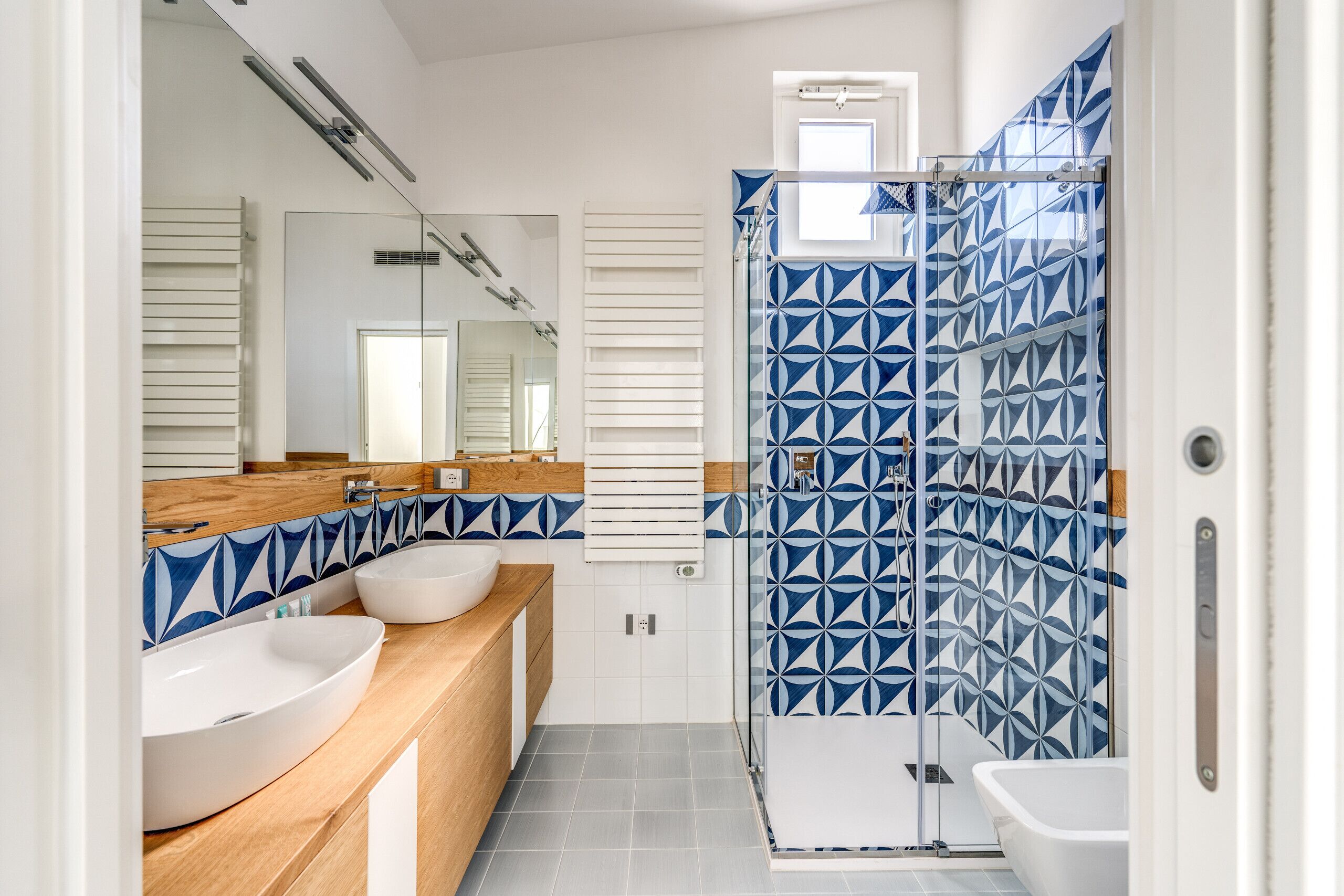 A modern bathroom with two sinks, a shower enclosure, and a large mirror.