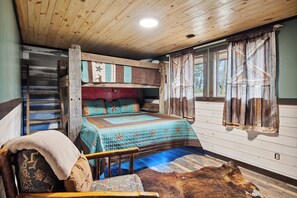 A rustic cabin interior with a wooden ceiling, a bed with patterned bedding, a wooden ladder, a window with curtains, and a fur rug on the floor. - Cozy Lodge w/Theater|Firepit|Arcade|Hot Tub (Gatlinburg)